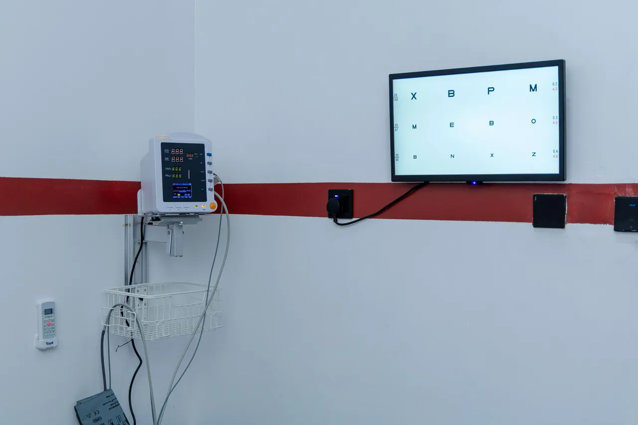Wall-mounted vital signs monitor beside a visual acuity chart screen
